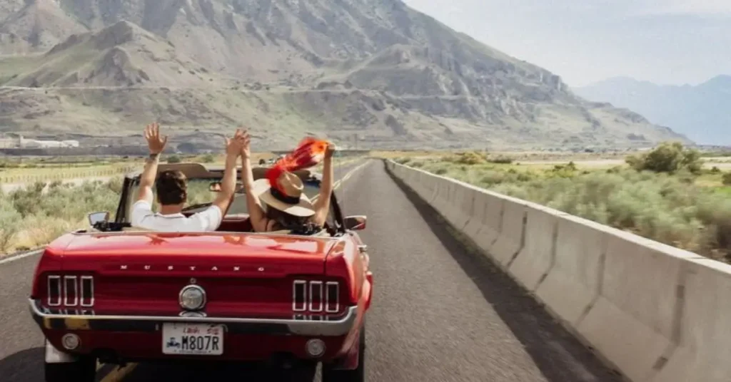 Vintage Convertible Cars Mustang with man and woman cheering their arms into the air 

